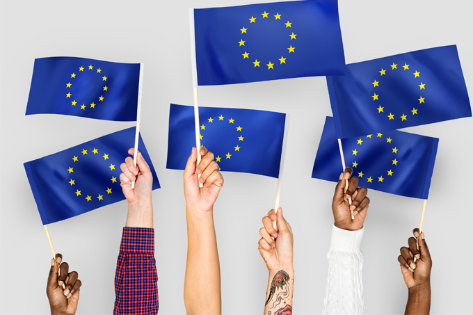 Kép:különböző nemzetiségű kezek uniós zászlókat tartanak a magasba