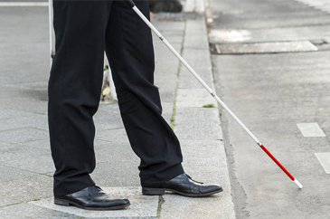 Egy öltönyös úr egy fehér bottal éppen átkell az úttesten