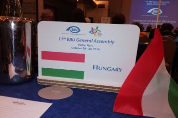 A magyar delegáció asztal táblája, mellette zászló, a háttérben EBU logó