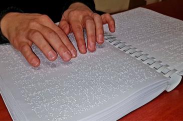 Nyitott Braille-könyv rajta kezek olvasnak